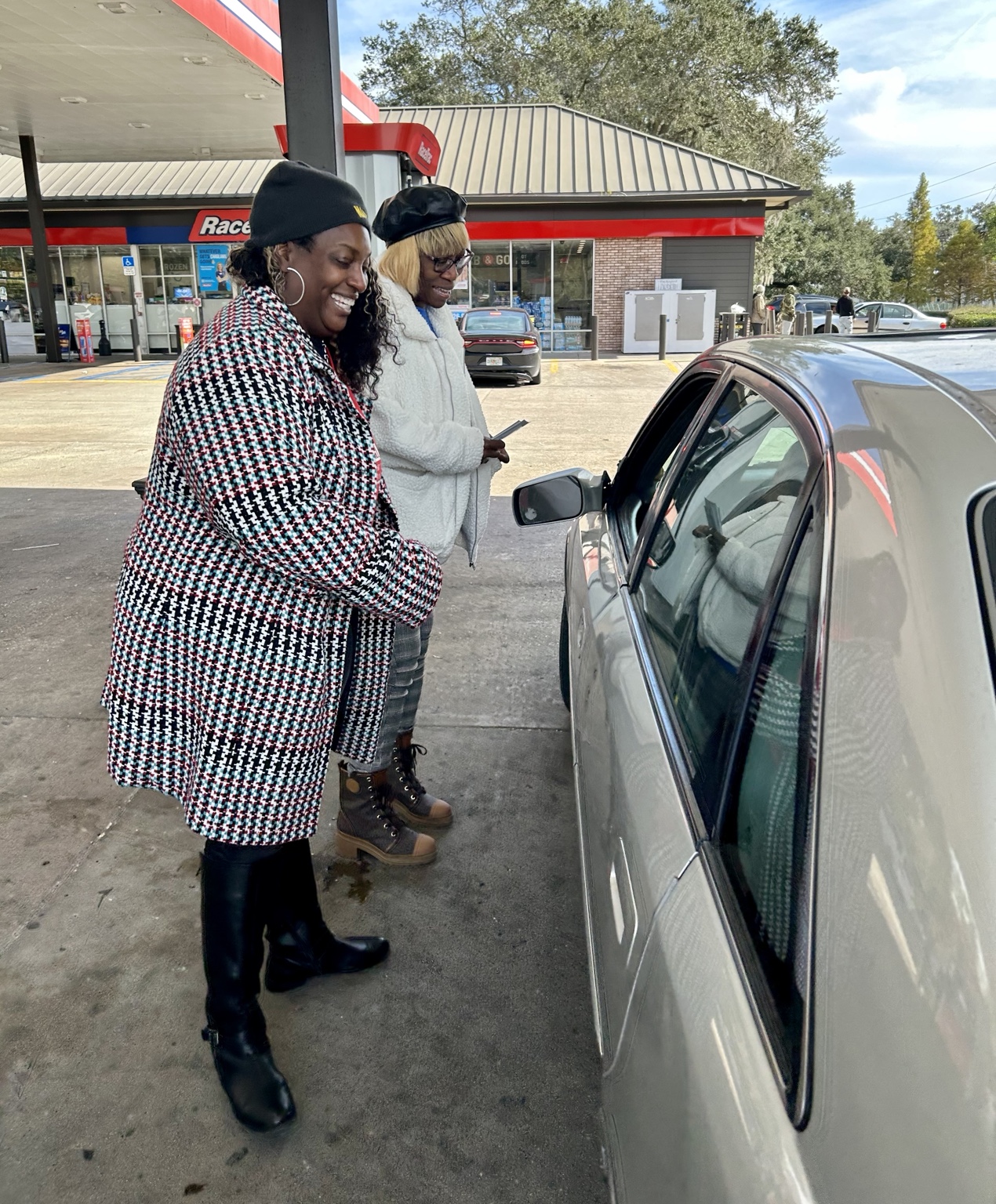 Two volunteers speaking with someone beside a car